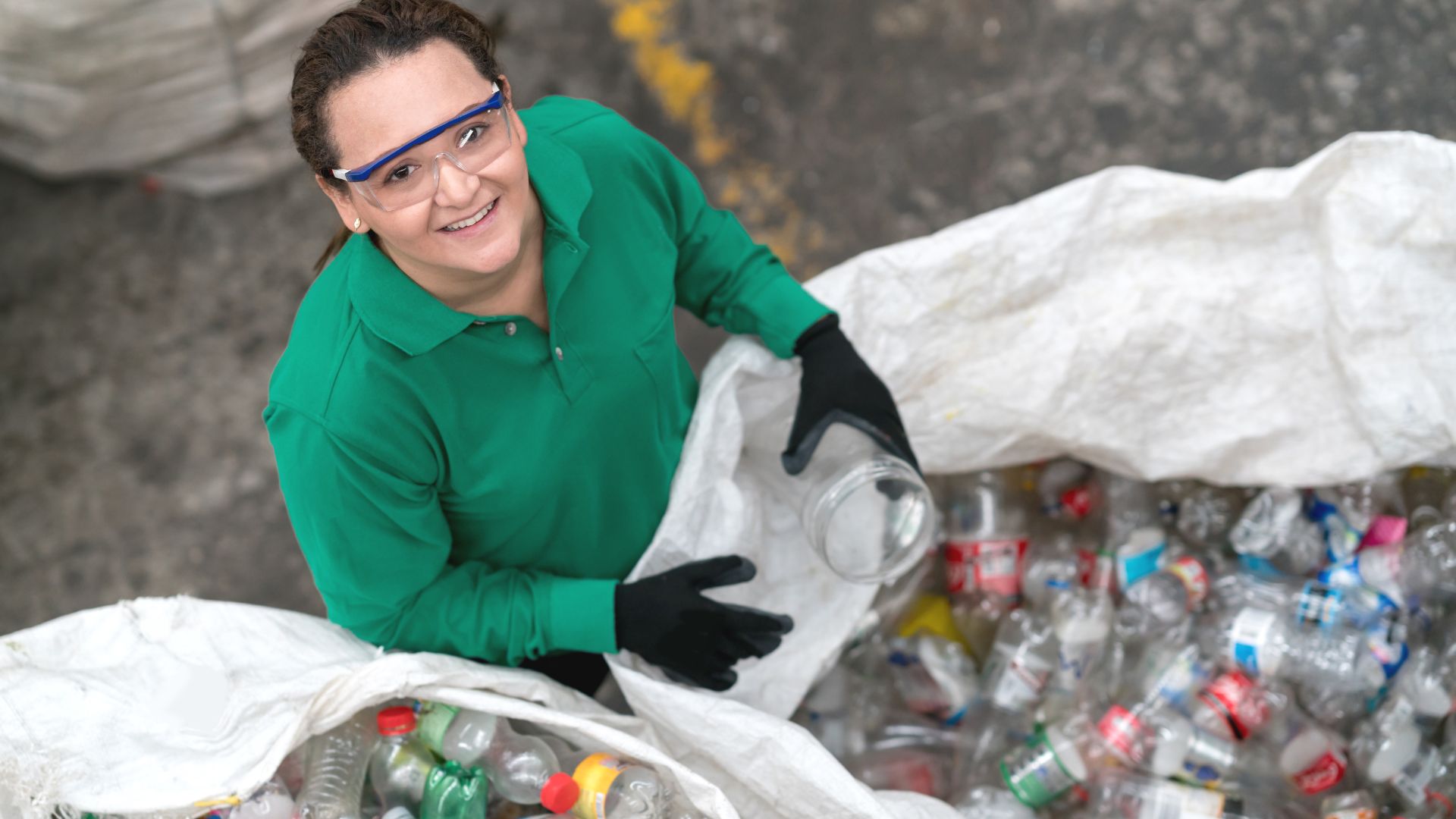 Smiling worker in green sorting recyclable plastic bottles at recycling facility